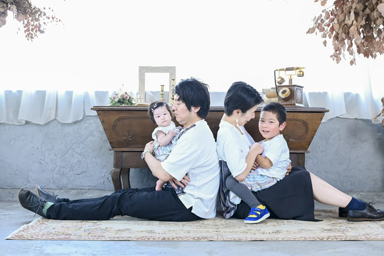 赤ちゃんを抱いたご家族が、上のお子さまと並んで座る家族写真|豊川店
