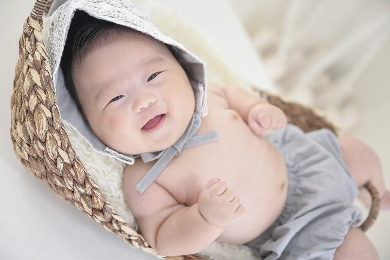 ニット帽をかぶり、かごの中で笑う赤ちゃん|豊橋店