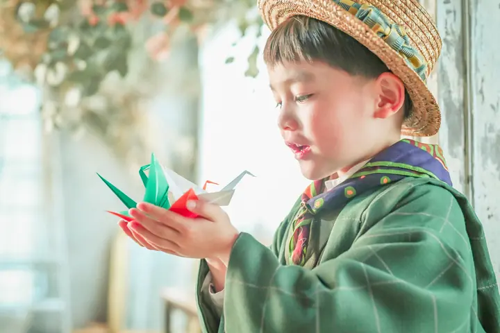 麦わら帽子の男の子が手のひらの折り鶴を見つめる