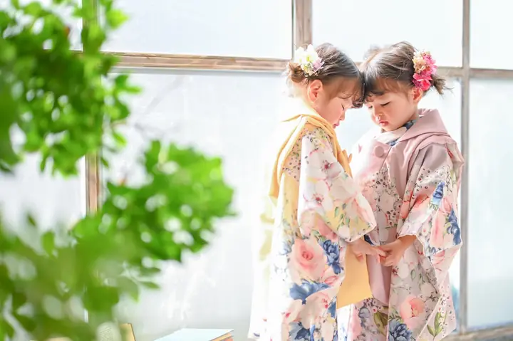 ピンクと黄色の被布を着た女の子2人がおでこを寄せ合う