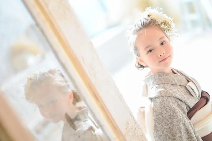 グレーの着物の女の子が鏡の横でほほえむ