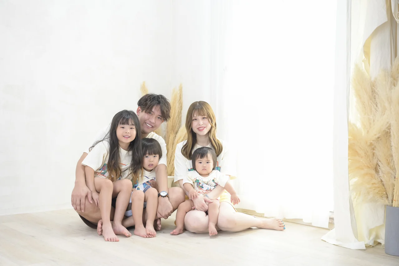 白い服をそろえ、窓辺で寄り添って座るご家族5人の写真|豊橋店