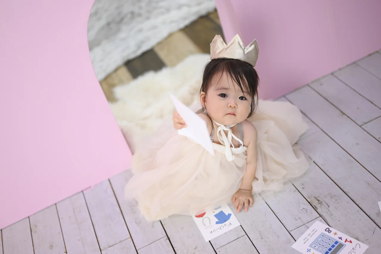 ピンクの背景で王冠と淡いドレスを身につけ、カードを手にするお子さま|豊橋店
